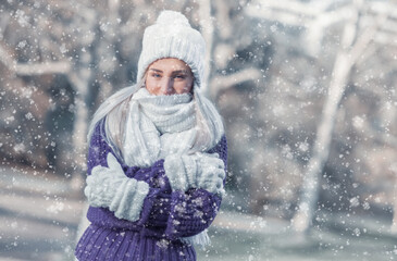 Fototapeta premium Portrait of happy woman in warm clothing on snowing winter day outdoors. Snowflakes falling on cheerful girl wearing wool cap, scarf and sweater