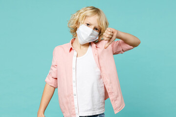 Little kid boy 10s in pink shirt sterile face mask safe from coronavirus virus covid-19 showing thumb down isolated on blue turquoise background children studio portrait. Childhood lifestyle concept.