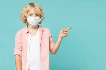 Little kid boy 10s in pink shirt sterile face mask safe from coronavirus virus covid-19 pointing index finger aside isolated on blue turquoise background studio portrait. Childhood lifestyle concept.