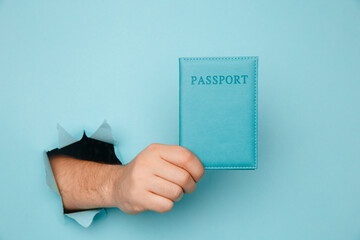 Traveler tourist man hand hold passport from a torn hole in blue paper.