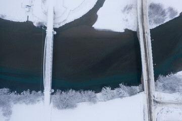 Bird's eye view of a car and a railroad bridge over the river Lech from above in the white snowy winter