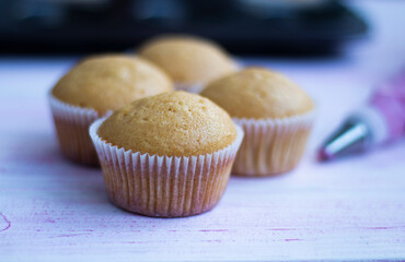 freshly baked muffins ready to be garnished, with a pastry bag filled with pink cream in the background. flour desserts. High quality photo