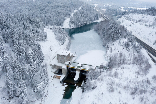Hydroelectric power station with weir system on the Lech river on the motorway in winter with snow-covered forest
