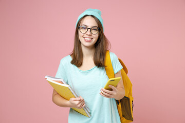 Cheerful young woman student in t-shirt hat glasses backpack hold notebooks using mobile cell phone...