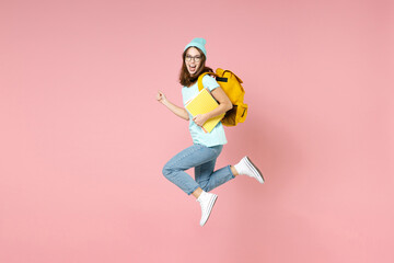 Full length side view of excited young woman student in blue t-shirt hat glasses backpack hold...