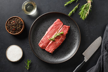 Raw marbled ribeye steak with rosemary sprig on black background. Top view.