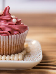 festive muffin with scarlet curd cream, pearl decor. the cupcake is decorated. Flour dessert with butter cream. muffin with cream on a saucer, stands on a wooden background . High quality photo. 