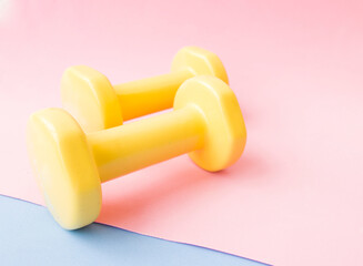 Yellow dumbbell color on pink, blue and yellow mat. Design of a sports poster or banner in fashionable colors of 2021