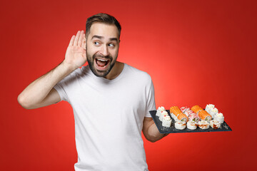 Curious young bearded man in white t-shirt try to hear you overhear listening intently hold...