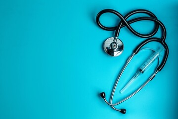 Medical stethoscope and syringe for injection on an aquamarine background. Medical care concept