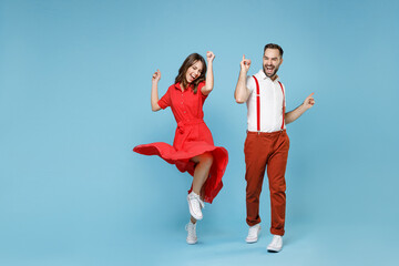 Full length of cheerful young couple friends man woman in white red clothes dancing point fingers up having fun isolated on pastel blue background studio portrait. St. Valentine's Day holiday concept.