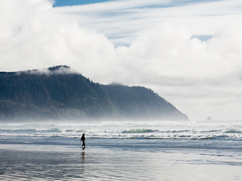 A cloudy day at the beach in Gearhart, Oregon. A lone figure walks out into the shallow waters as the tides recede.