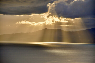The sun behind the clouds with rays of light shining down on sea. Rays of sun peeking through...