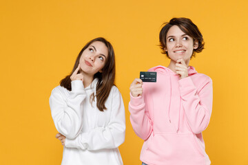 Pensive two young women friends 20s wearing casual white pink hoodies standing hold credit bank...