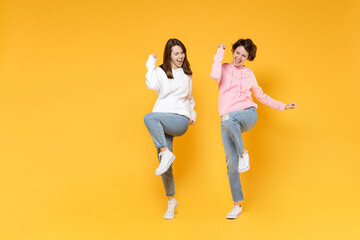 Fototapeta na wymiar Full length of overjoyed two young women friends 20s wearing basic white pink hoodies doing winner gesture celebrating clenching fists say yes isolated on bright yellow background studio portrait.