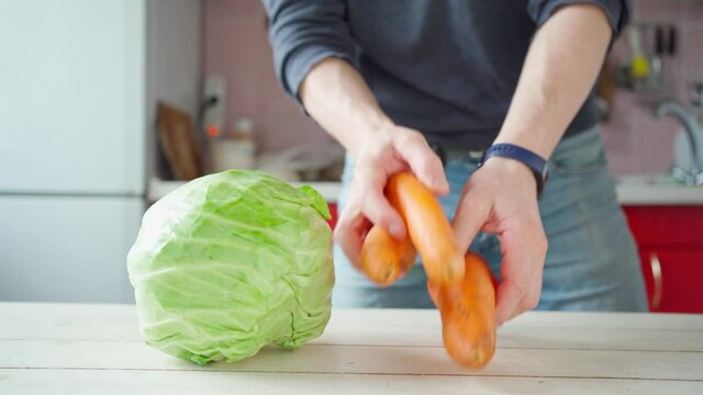 man puts fresh vegetables on wooden table on kitchen. kale, carrots, cucumbers, radishes, spinach parsley ingredients for healthy vegetarian salad. organic products, preparing delicious healthy food.