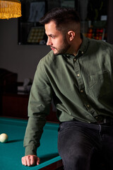 male in casual wear sits on billiards table, looking at game, snooker sport game concept. portrait