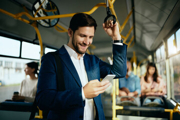 Happy businessman texting on cell phone while commuting to work by bus. - obrazy, fototapety, plakaty