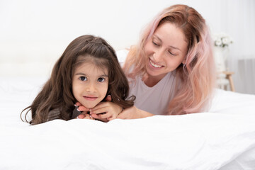 mother play with little active daughter in bed at home, having fun, activity with children