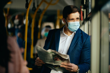 Male entrepreneur reading newspaper and wearing face mask while commuting by bus.
