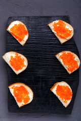 Bruschettes with butter and red caviar laid out on a black board on a gray concrete background copy space.