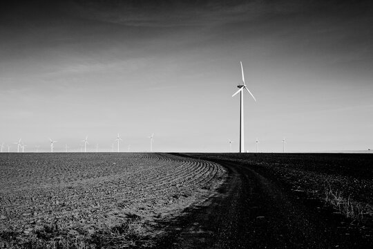 A lone windmill in the foreground with a line of windmills off in the distance in this black and white image.  An otherwise empty landscape.