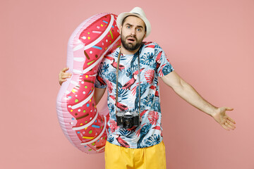 Confused young traveler tourist man in summer clothes hat photo camera hold inflatable ring spreading hands isolated on pink background. Passenger traveling on weekends. Air flight journey concept.