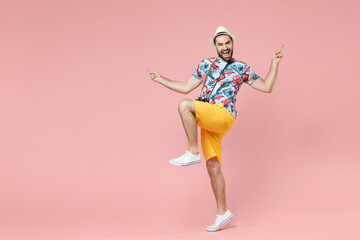 Full length of laughing young traveler tourist man in summer clothes hat point index fingers up dancing isolated on pink background studio. Passenger traveling on weekends. Air flight journey concept.