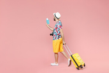 Full length side view of young traveler tourist man in summer clothes hat hold suitcase passport tickets isolated on pink color background. Passenger traveling on weekends. Air flight journey concept.