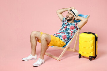 Full length of funny young traveler tourist man in summer clothes hat sit on deck chair put hands...