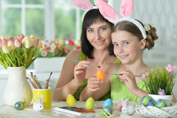 happy mother with daughter wearing rabbit ears decorating  Easter eggs