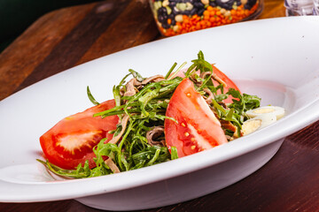 Beef tongue salad with arugula, tomatoes and quail egg on white plate