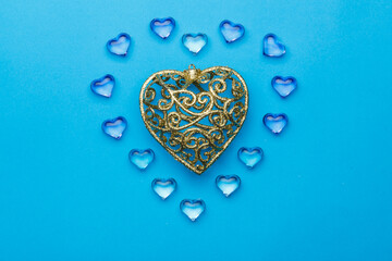 On a blue background, there is a heart made of transparent pebbles in the shape of hearts in the middle of a golden heart.