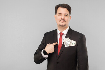 Businessman pointing finger at himself money in the pocket. Indoor, studio shot, isolated on gray background