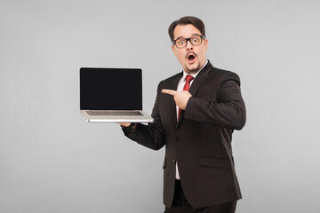 Business, gadgets,technologies. Businessman with amazement face showing new note book. Indoor, studio shot, isolated on gray background