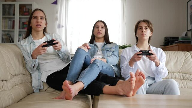 Teenager girls at home triplet sisters have fun play console games sitting on couch at home stay isolated under quarantine