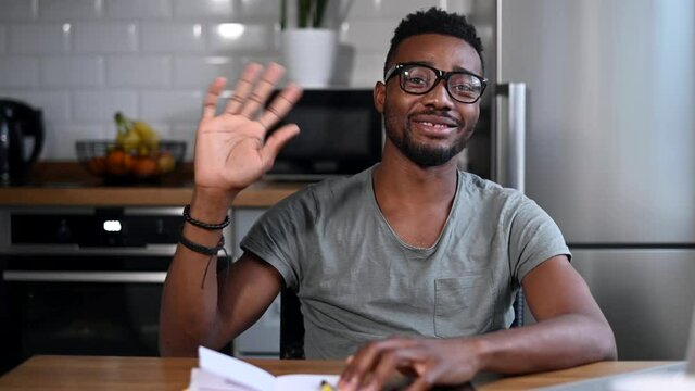 Headshot of cheerful African-American man talking online, waving hand, saying hello and looks at camera with a pleasant smile, video call, virtual meeting, remote interview