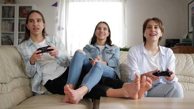 Teenager girls at home triplet sisters have fun play console games sitting on couch at home stay isolated under quarantine