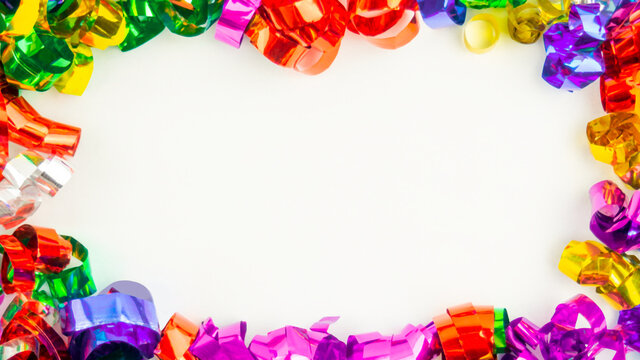 Closeup frame of colorful holiday metal ribbons on white.Christmas,New Year,birthday foil serpentine decoration.Festive party decor.Invitation rattern,greeting card design.Horizontal banner,copy space