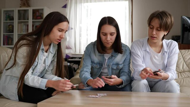 Teenager triplet sisters girls play cards board game for family fun at home