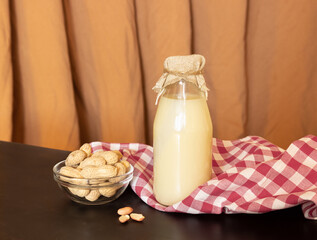Peanut milk in a glass bottle and peanuts in a shell on a background of fabric with pleats....