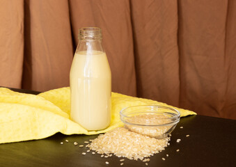 Rice milk in a glass bottle and white rice on a background of fabric with pleats. Vegetable milk,...