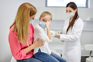Obraz premium female doctor taking blood sample test of a little girl in the clinic, scared girl sits with mother, woman technician making blood tests on child in the laboratory of blood extractions