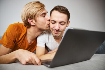 Happy gay couple using laptop and sharing tender kiss