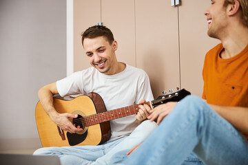 Cheerful male guitarist spending time with boyfriend at home