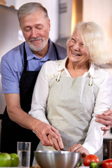 elderly couple preparing vegetable salad in kitchen, gray-haired handsome man helps wife with cooking, going to have healthy breakfast. focus on hands