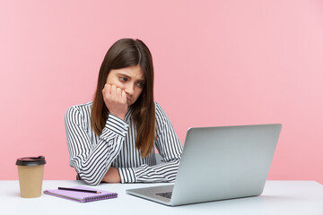 Exhausted bored woman office worker looking at laptop screen with sadness, leaning on arm, feeling lazy uninterested in her job, depression at work. Indoor studio shot isolated on pink background
