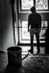 a metal mug stands on a concrete staircase stands, in the background a homeless man