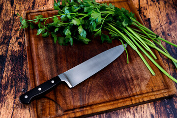 Worn wooden cutting board on an old worn wooden table with a knife on it and parsley