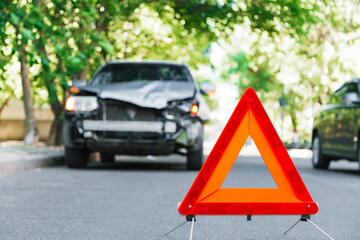 Red emergency stop triangle sign on road during a car accident. Broken gray car in road traffic accident. Car crash traffic accident on city road after collision